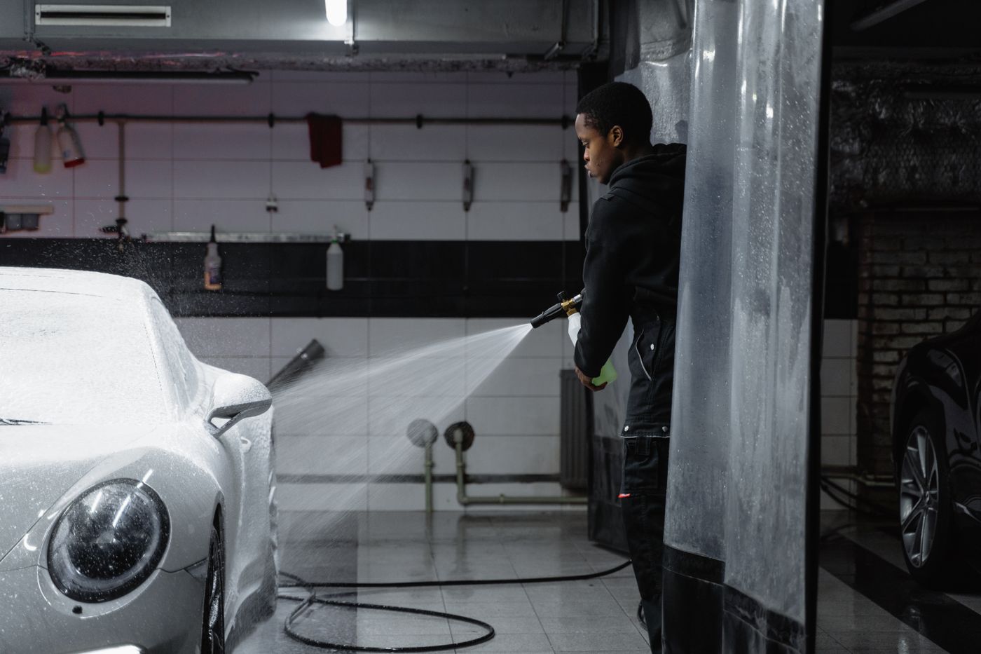 Laveur de l'équipe pulvérisant la mousse active sur une berline, station de lavage Clean Car Galsen